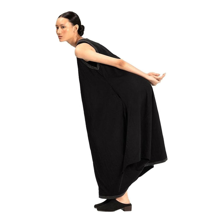 Model wearing an Anaabu black sleeveless midi dress with a voluminous A-line silhouette, asymmetric handkerchief hemline, and fine metallic stud trim at the neckline and hem - packshot