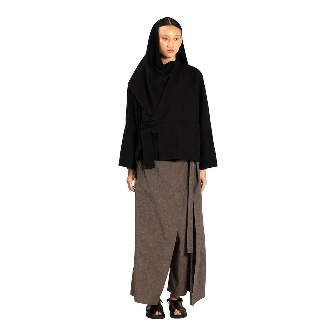 Model wearing the Anaabu Shawl Jacket in black — a draped wrap-style jacket with oversized shawl collar and self-tie belt, styled over a black turtleneck and olive wide-leg trousers - packshot