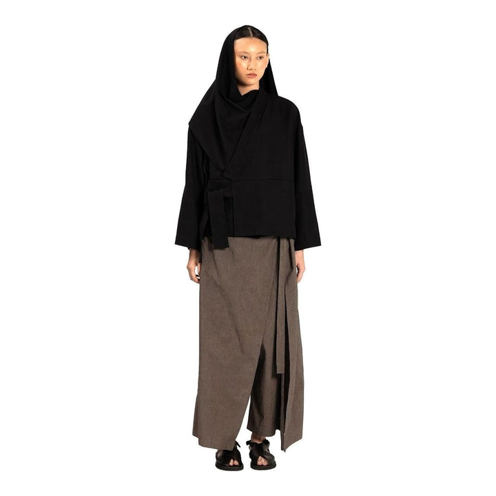 Model wearing the Anaabu Shawl Jacket in black — a draped wrap-style jacket with oversized shawl collar and self-tie belt, styled over a black turtleneck and olive wide-leg trousers - packshot