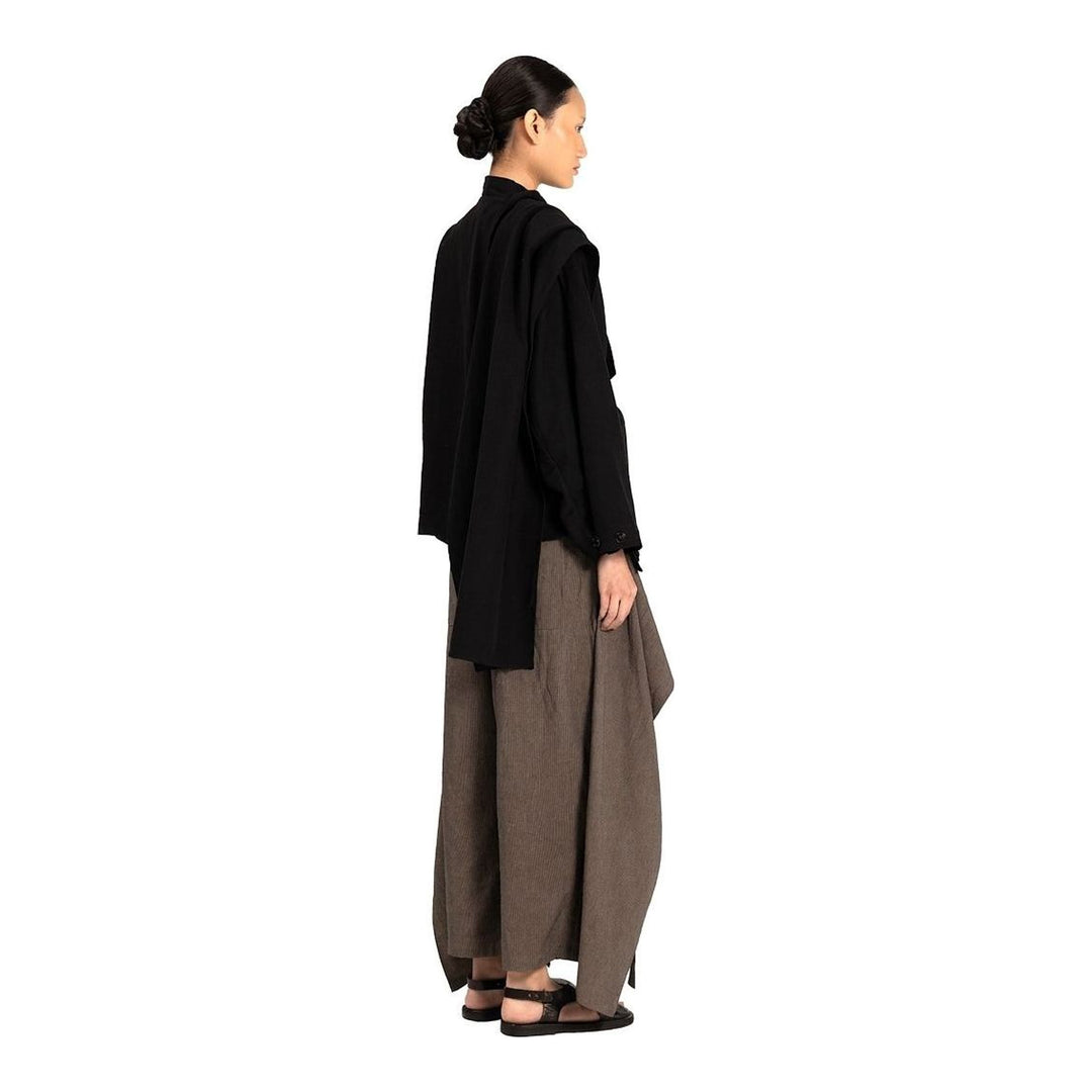Model wearing the Anaabu Shawl Jacket in black — a draped wrap-style jacket with oversized shawl collar and self-tie belt, styled over a black turtleneck and olive wide-leg trousers - packshot