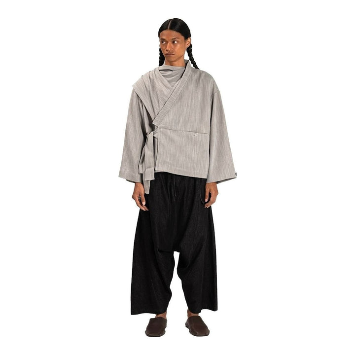 Model wearing the Anaabu Shawl Jacket in black — a draped wrap-style jacket with oversized shawl collar and self-tie belt, styled over a black turtleneck and olive wide-leg trousers - packshot