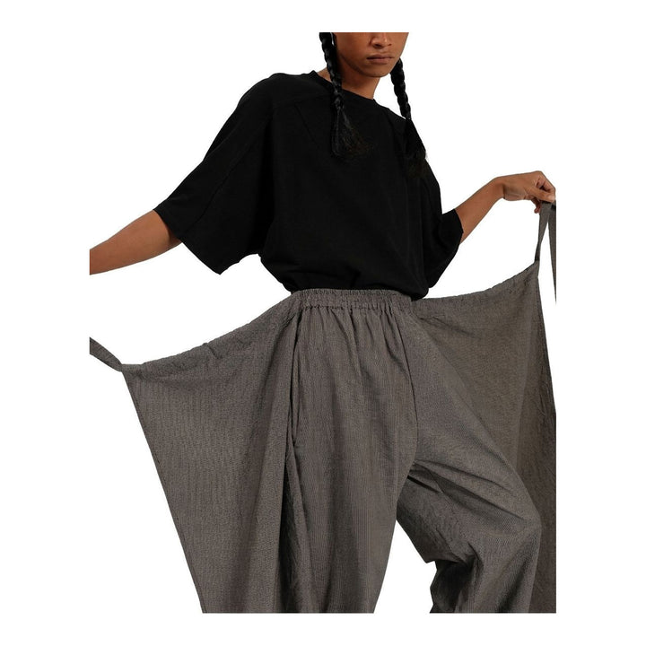 Model wearing Anaabu The Skants — black wide-leg cropped pants with large draped overlay panels featuring pinstripe and dot print, paired with a black square-neck crop top and leather sandals - packshot
