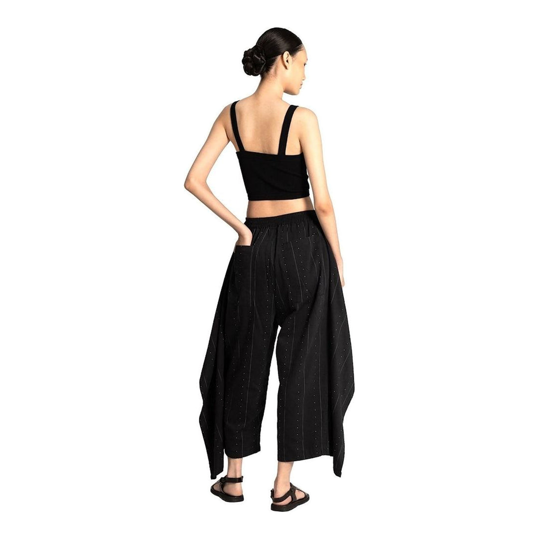 Model wearing Anaabu The Skants — black wide-leg cropped pants with large draped overlay panels featuring pinstripe and dot print, paired with a black square-neck crop top and leather sandals - packshot