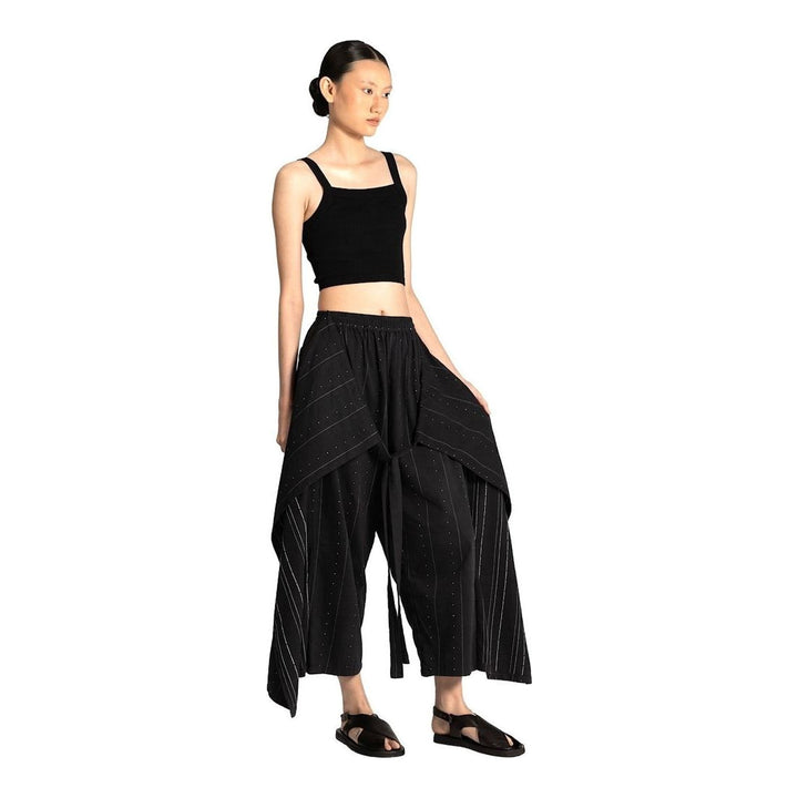 Model wearing Anaabu The Skants — black wide-leg cropped pants with large draped overlay panels featuring pinstripe and dot print, paired with a black square-neck crop top and leather sandals - packshot