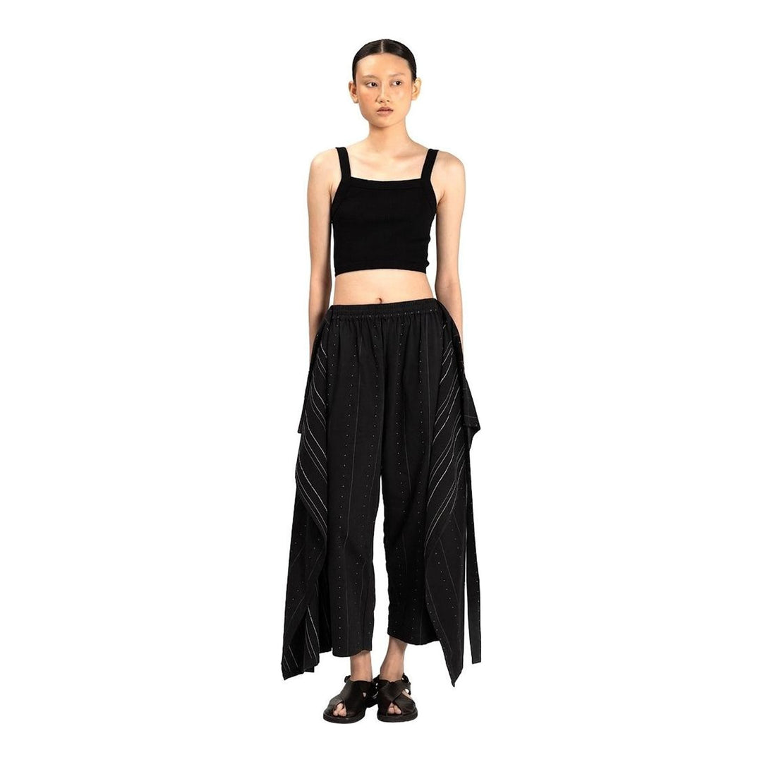 Model wearing Anaabu The Skants — black wide-leg cropped pants with large draped overlay panels featuring pinstripe and dot print, paired with a black square-neck crop top and leather sandals - packshot