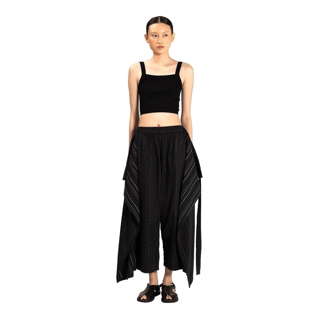 Model wearing Anaabu The Skants — black wide-leg cropped pants with large draped overlay panels featuring pinstripe and dot print, paired with a black square-neck crop top and leather sandals - packshot