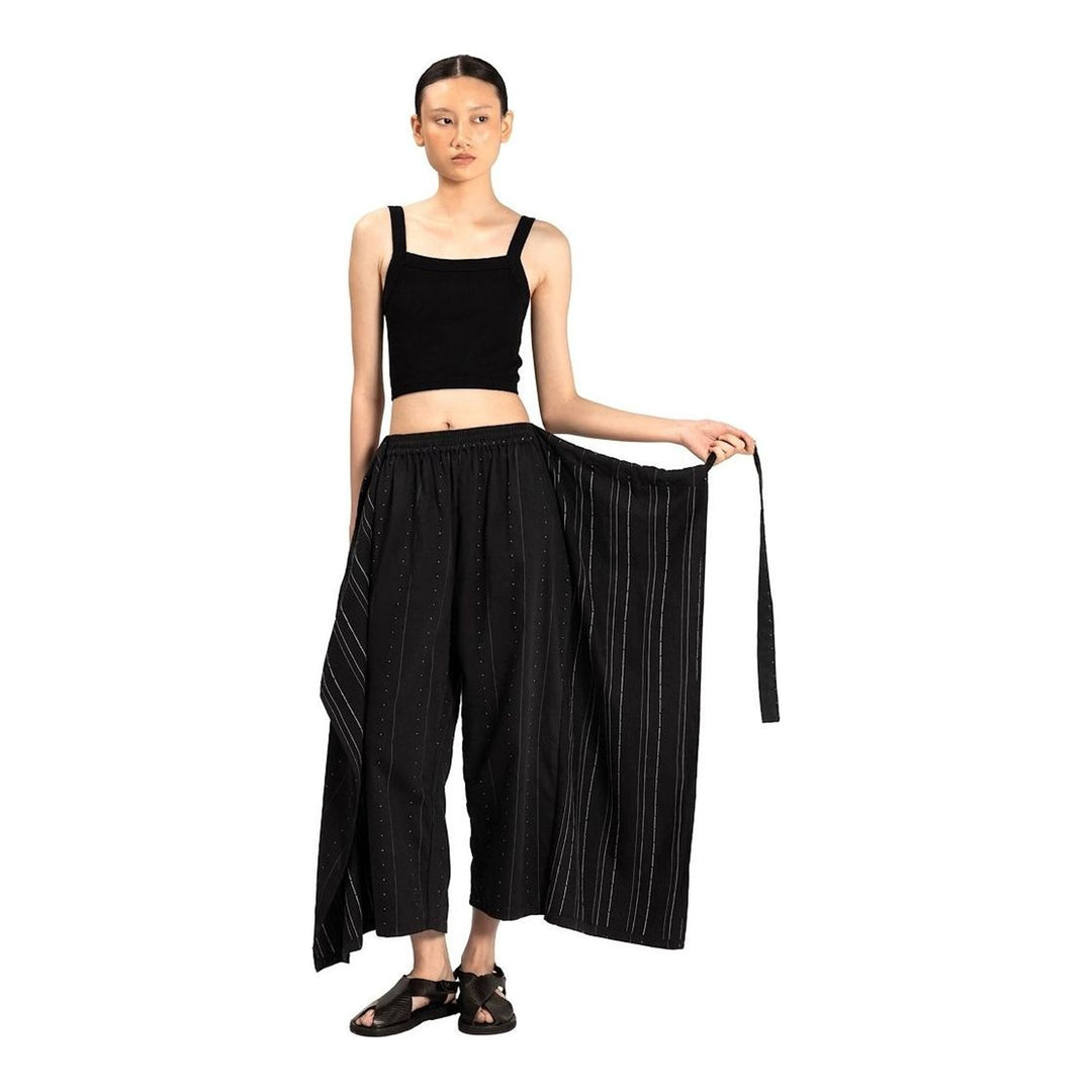 Model wearing Anaabu The Skants — black wide-leg cropped pants with large draped overlay panels featuring pinstripe and dot print, paired with a black square-neck crop top and leather sandals - packshot