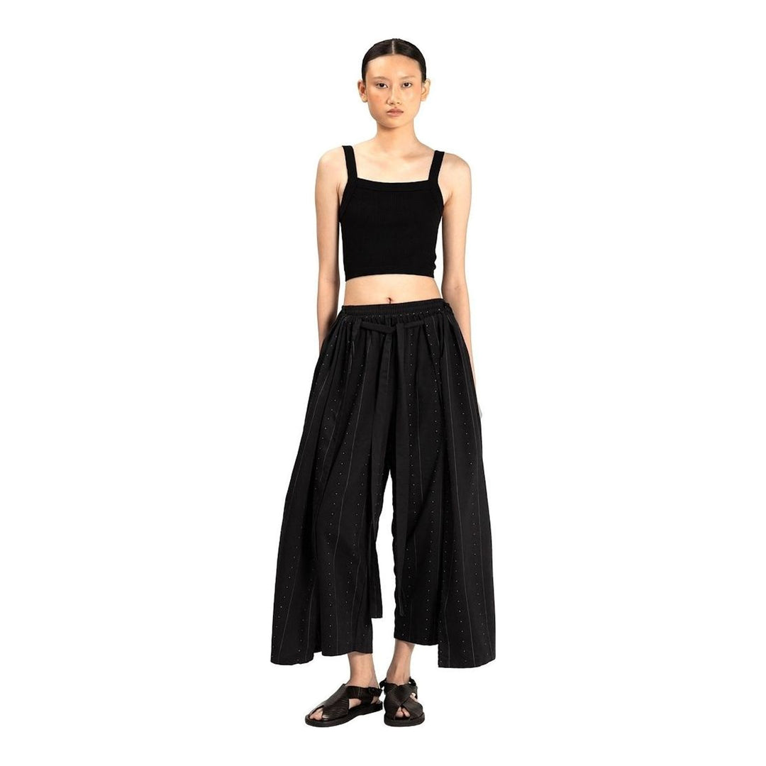 Model wearing Anaabu The Skants — black wide-leg cropped pants with large draped overlay panels featuring pinstripe and dot print, paired with a black square-neck crop top and leather sandals - packshot