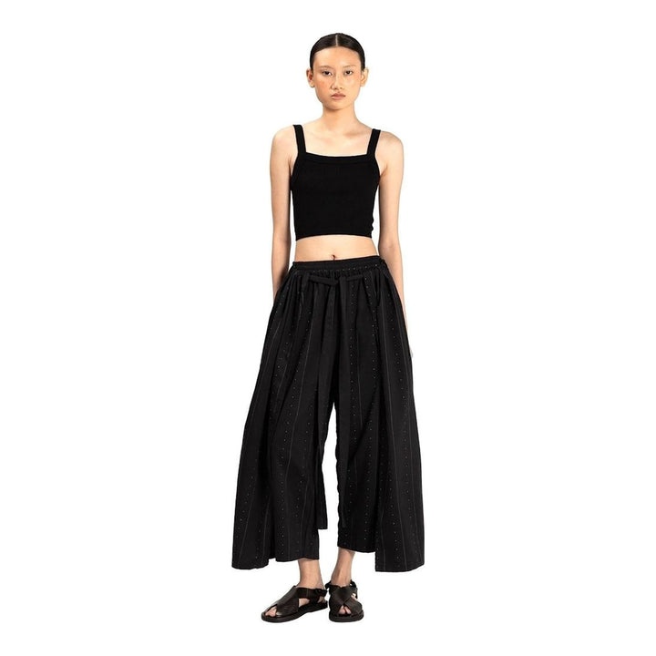 Model wearing Anaabu The Skants — black wide-leg cropped pants with large draped overlay panels featuring pinstripe and dot print, paired with a black square-neck crop top and leather sandals - packshot