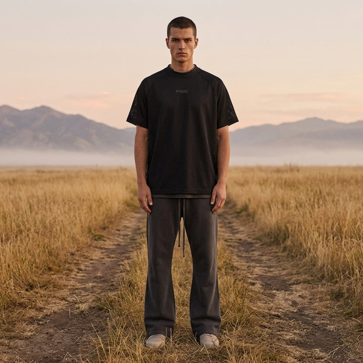 Fear of God Essentials Essential Raglan Tee in black with tonal FGE logo on the chest and ribbed crewneck, shown flat from the front - lifestyle