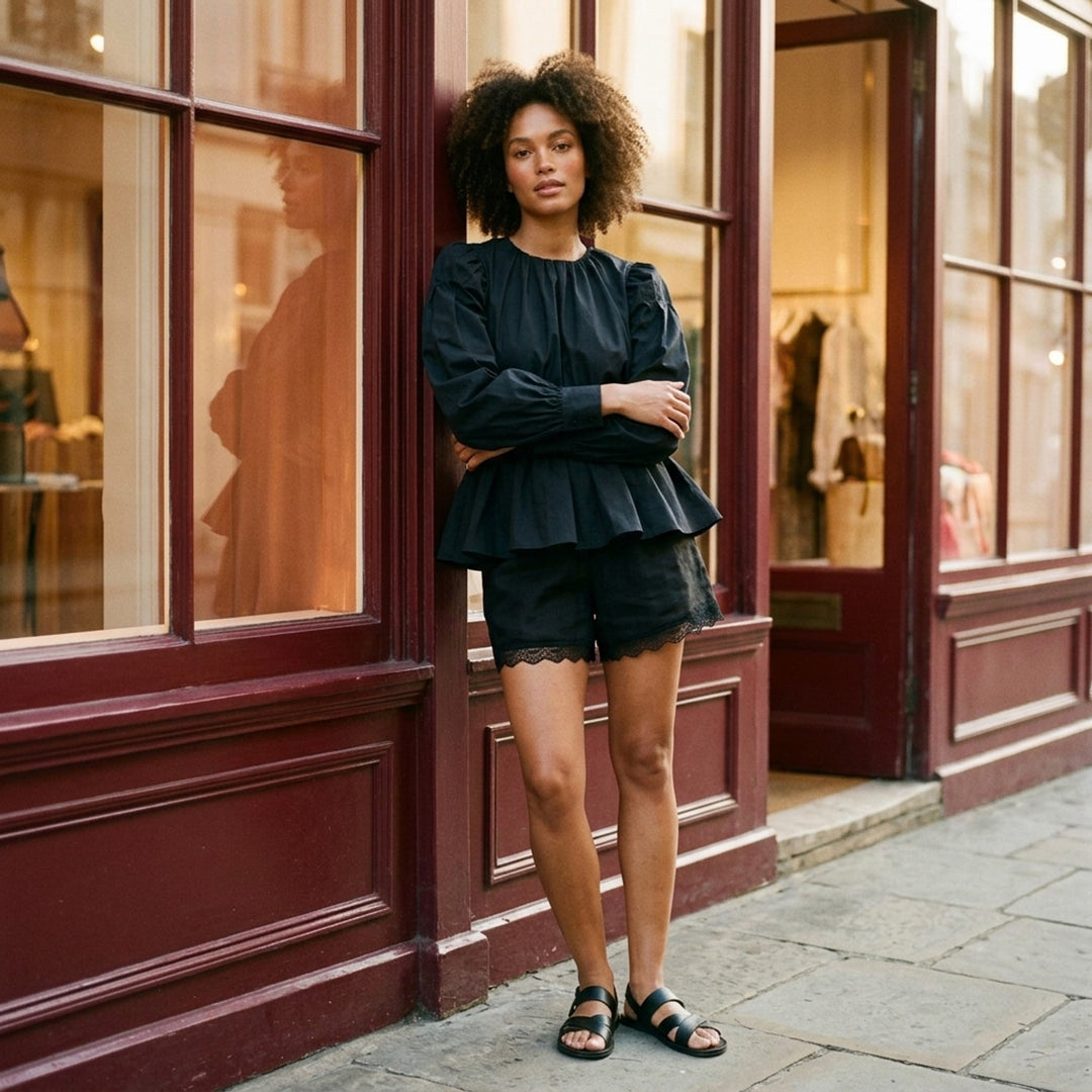 Ganni Compact Poplin Gathered Peplum Top in black, featuring a ruched neckline, voluminous long sleeves with elasticated cuffs, and a flared peplum hem with elasticated waistband - lifestyle