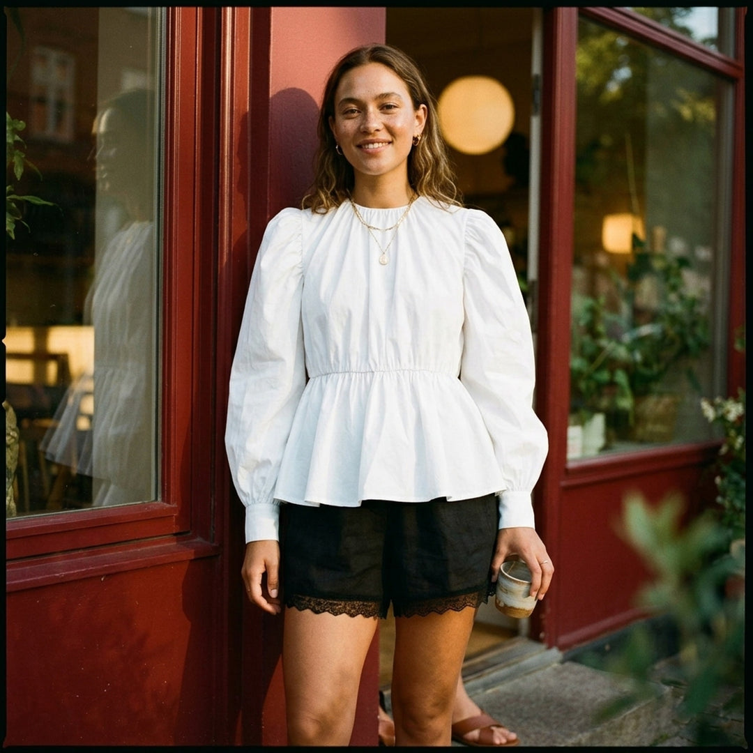 Ganni Compact Poplin Gathered Peplum Top in black, featuring a ruched neckline, voluminous long sleeves with elasticated cuffs, and a flared peplum hem with elasticated waistband - lifestyle