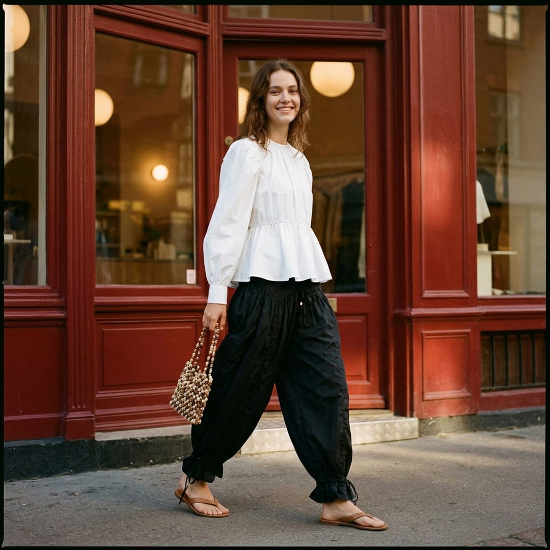 Ganni Flyweight Nylon Balloon Pants in black, featuring a smocked yoke, voluminous gathered body, and ruched tie ankles, displayed flat on a white background - lifestyle