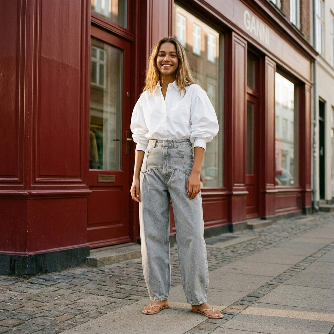 Ganni Rigid Denim Corset Jeans in light grey, featuring a high-rise waist, ruched corset seaming at the hip, and a wide balloon-leg silhouette tapering to small hem vents — front view on white background - lifestyle