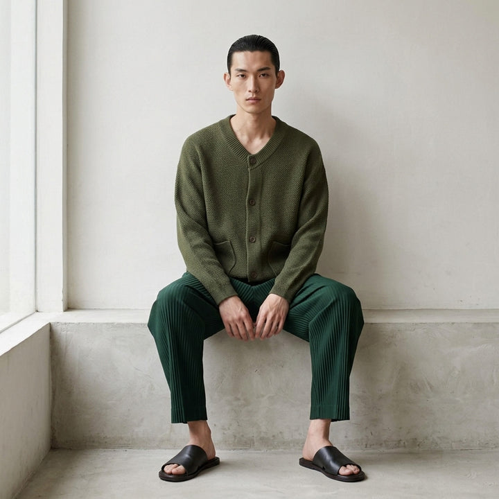 Homme Plissé Issey Miyake Rustic Knit Cardigan in charcoal, featuring a ribbed V-neckline, tonal button-through front, pebbled knit body, and two smooth-panel patch pockets at the hem - lifestyle