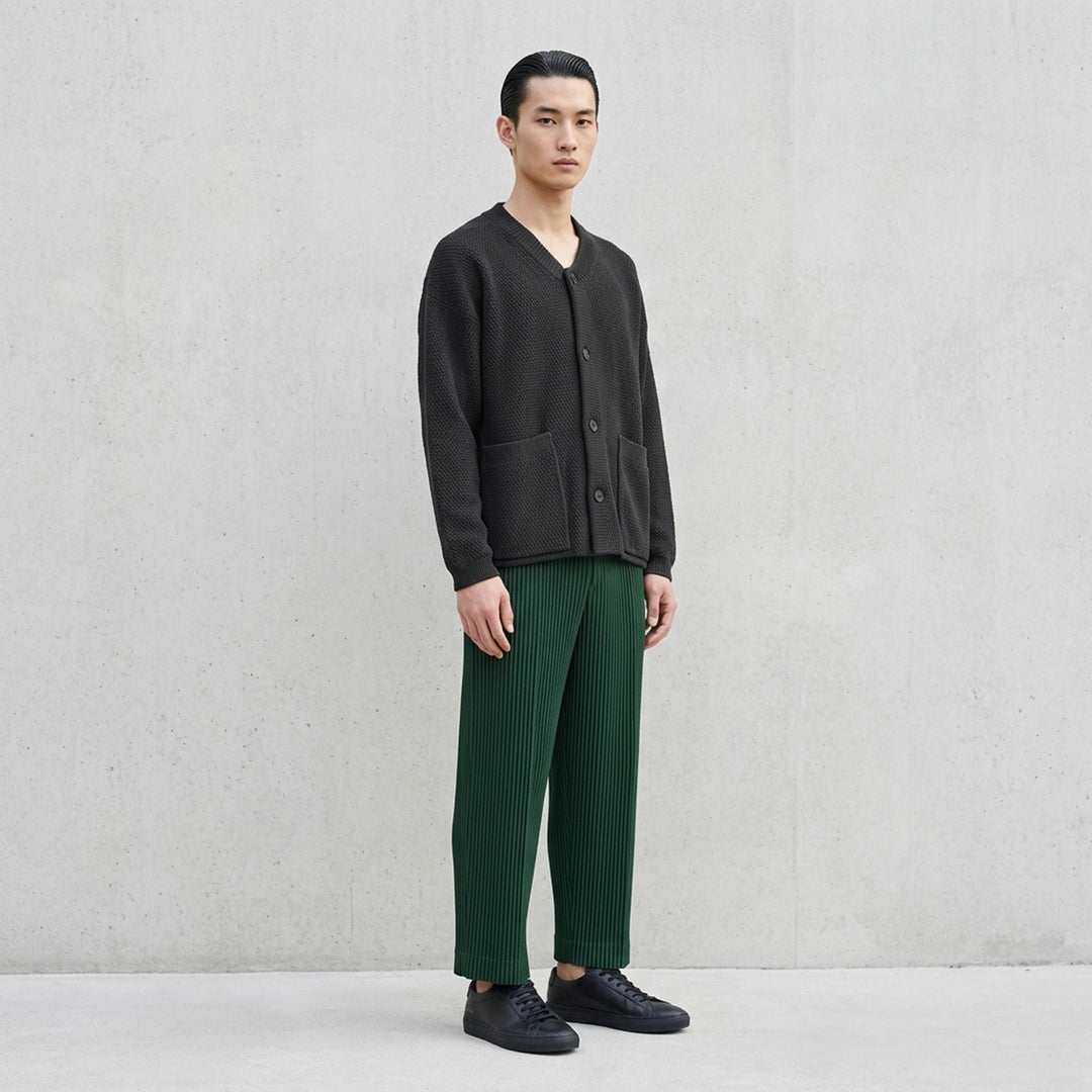Homme Plissé Issey Miyake Rustic Knit Cardigan in charcoal, featuring a ribbed V-neckline, tonal button-through front, pebbled knit body, and two smooth-panel patch pockets at the hem - lifestyle
