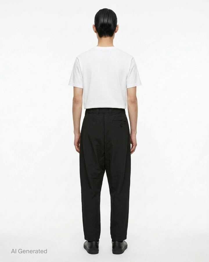 IM Men Cotton Yak Woven Pants in black — high-rise pleated drop-crotch trousers with a cropped tapered hem, front view on white background - back