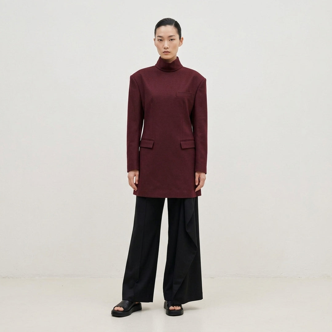 Issey Miyake burgundy tunic with funnel neck, structured shoulders, chest welt pocket and two flap pockets, shown from the front - lifestyle