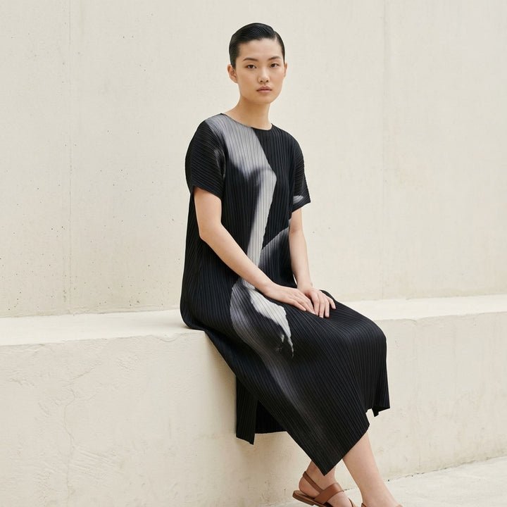Issey Miyake Hands of Lover Pleats short-sleeve midi dress in black with abstract monochromatic photographic print and asymmetric hem, shown on a plain white background - lifestyle
