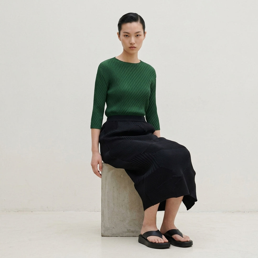Issey Miyake KONE KONE black sculptural ribbed knit skirt with three-dimensional alternating pleated panels and an asymmetric hem, shot flat on a white background - lifestyle