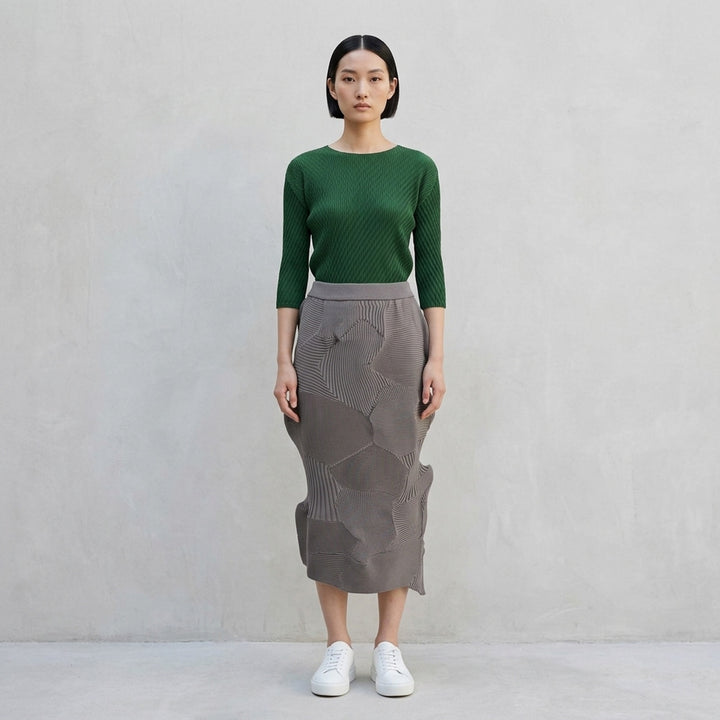 Issey Miyake KONE KONE black sculptural ribbed knit skirt with three-dimensional alternating pleated panels and an asymmetric hem, shot flat on a white background - lifestyle