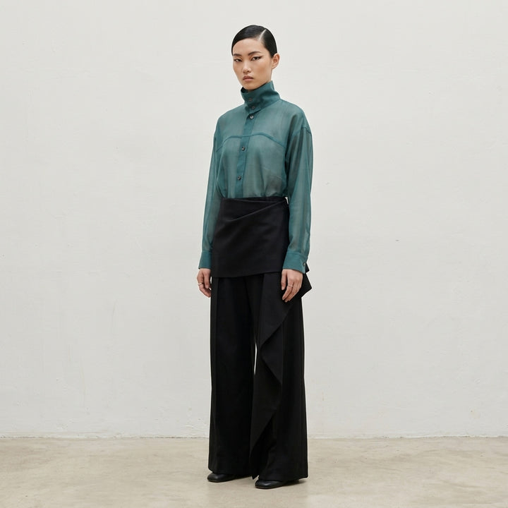 Issey Miyake Lustrous Wool Pants in black, featuring a wide-leg silhouette and asymmetric draped skirt overlay cascading from the high waist - lifestyle