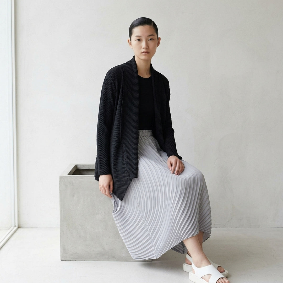 Issey Miyake Misty Pleats black pleated open-front cardigan, rear view, showing draped lapel collar, textured pleated fabric, long sleeves, and asymmetric hem - lifestyle