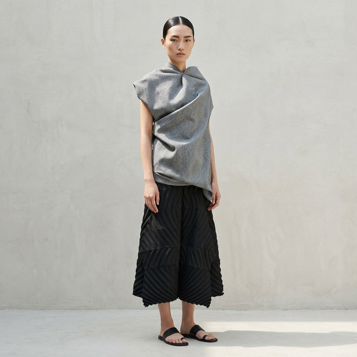 Issey Miyake Reflection woven top in heathered grey, shown flat displaying its asymmetric draped and gathered sculptural silhouette with open-weave textured fabric and visible brand label at neckline - lifestyle