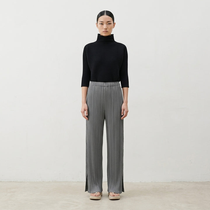Pleats Please Issey Miyake Mellow Pleats Pants in black — wide-leg cropped silhouette with vertical micro-pleating, elasticated waistband, and side-slit hem, shown flat on white background - lifestyle