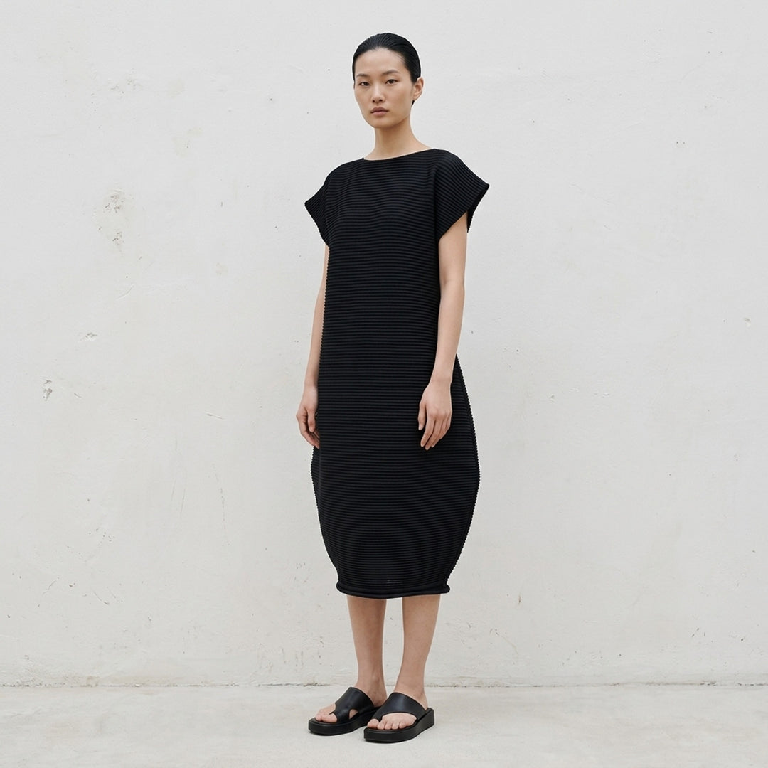 Pleats Please Issey Miyake Zig Zag Knit Dress in black, featuring horizontal ribbed pleating, cap sleeves, and a sculpted tulip-shaped skirt, shown from the back on a white background - lifestyle